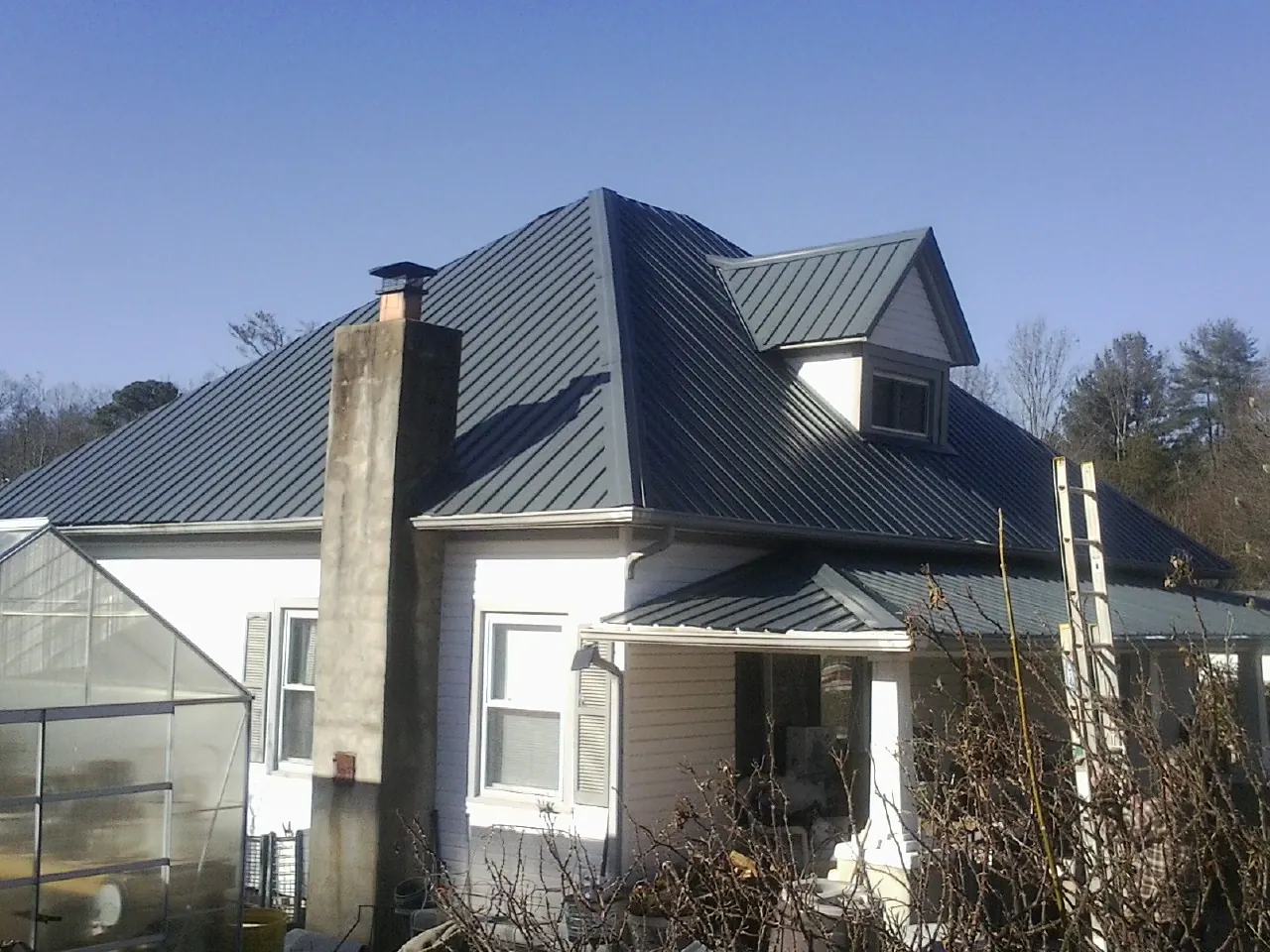 Dark blue standing seam metal roof on a white farmhouse with dormer — Slate & Tile Roof Repair by Roofing Brothers in Atlantic Beach
