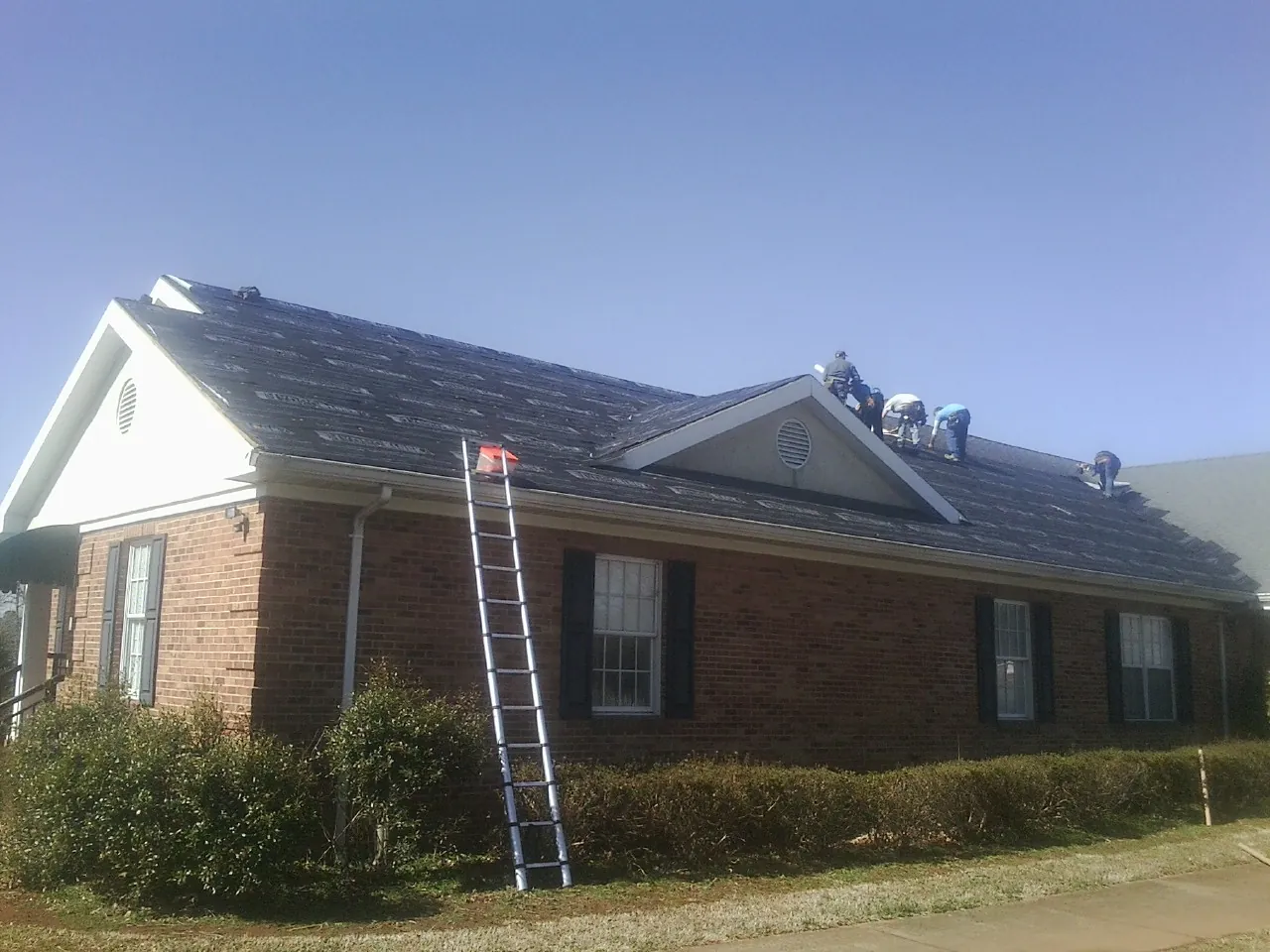 Crew tearing shingles off a brick ranch roof with a ladder set — Metal Roof Repair work by our crew in Atlantic Beach